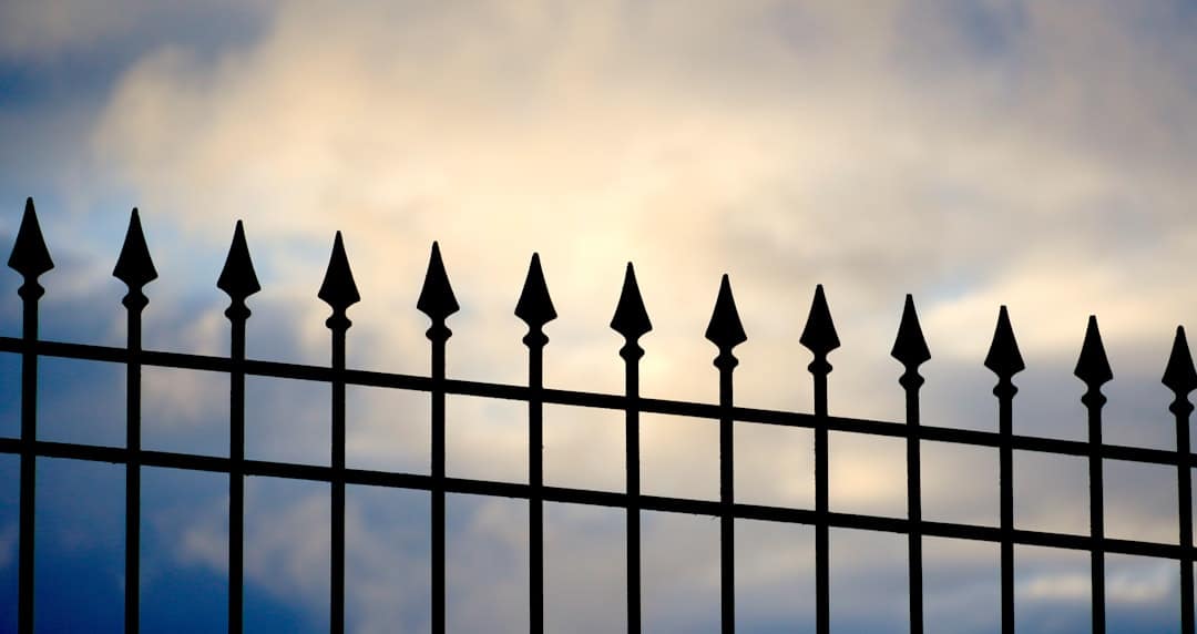about-01 a-black-iron-fence-with-a-cloudy-sky-in-the-background-nhtdgytgzky